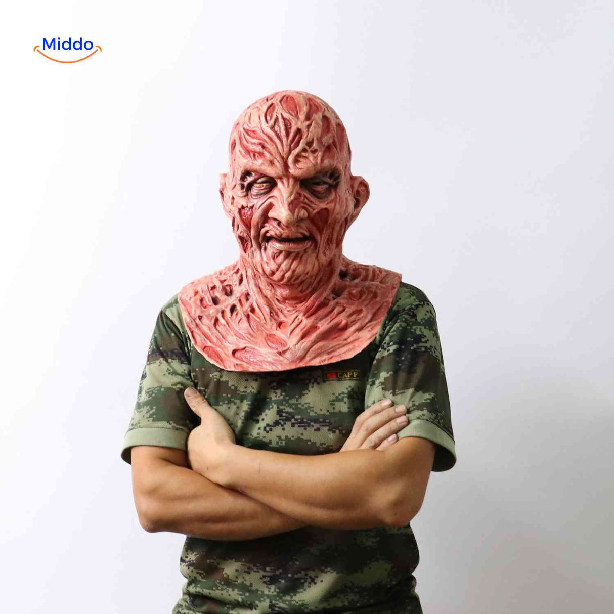 Zombiora-Maske: Person trägt eine verbrannte Gesichtsmaske mit Camo-Shirt und verschränkten Armen. Besuchen Sie uns auf www.middo.de
