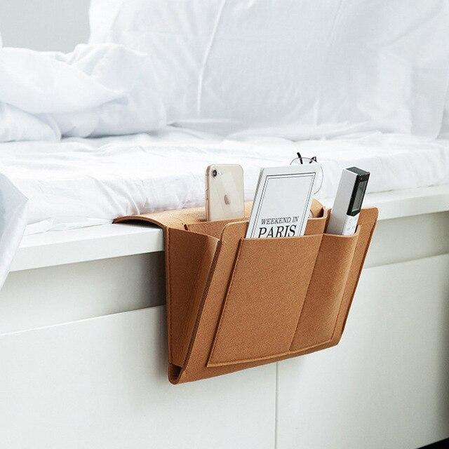 Foto von der braunen Leder-BedCaddy, die an einem weißen Bett hängt, mit Sachen darin.
