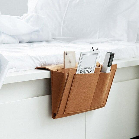 Foto von der braunen Leder-BedCaddy, die an einem weißen Bett hängt, mit Sachen darin
