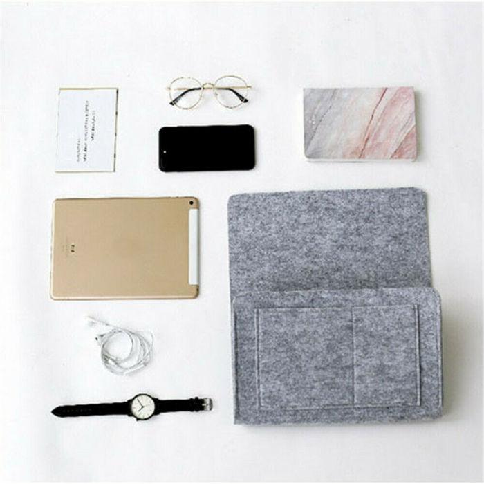 Foto von einem hellgrauen BedCaddy, der auf einem weißen Untergrund liegt, daneben ein Uhrenladekabel, ein Telefon, eine Brille und ein Notizbuch