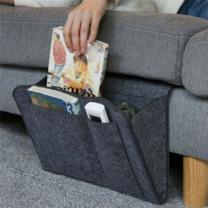 Ein graues BedCaddy mit zwei Büchern und einer Fernbedienung hängt an der Seite einer grauen Couch