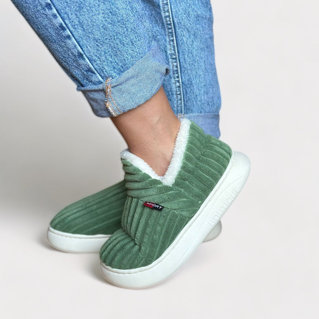 Person trägt grüne CozyComfort Fleece Hausschuhe mit weißem Fleece-Futter und weißer Sohle.