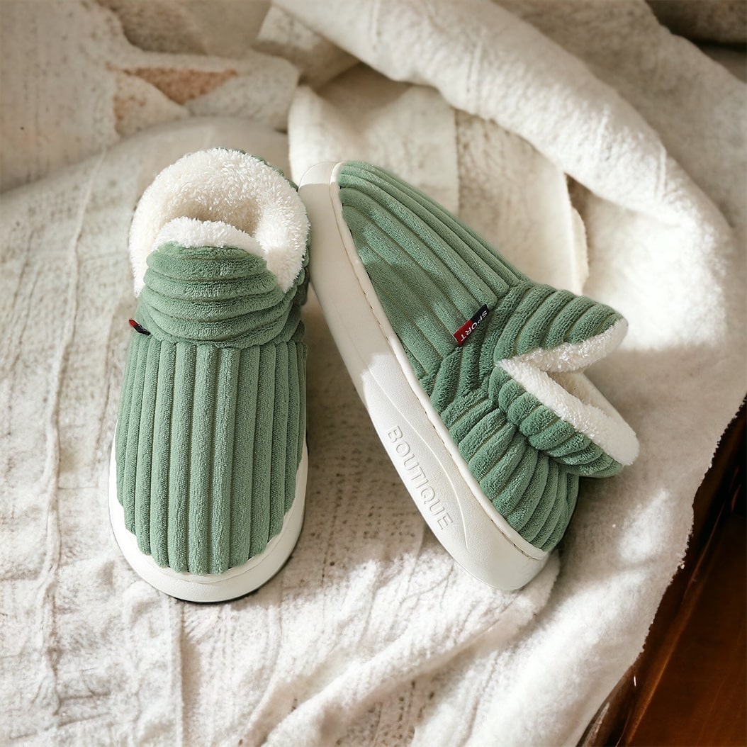 Grüne Fleece Hausschuhe mit weißem Fleece-Futter, liegend auf einer weißen, weichen Decke.
