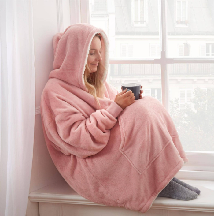 Eine Person trägt einen rosa Sherpa-Fleece-XXL-Hoodie, entspannt zu Hause.