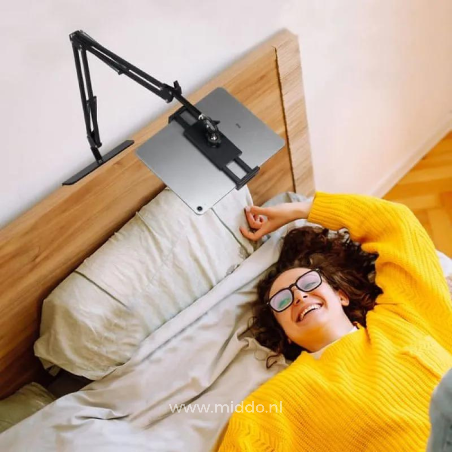 Frau liegt im Bett mit einem FlexArm Tablethalter, der am Kopfteil des Bettes befestigt ist.