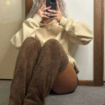 Modell in braunen FluffSocks, sitzend auf dem Boden mit einem Telefon.