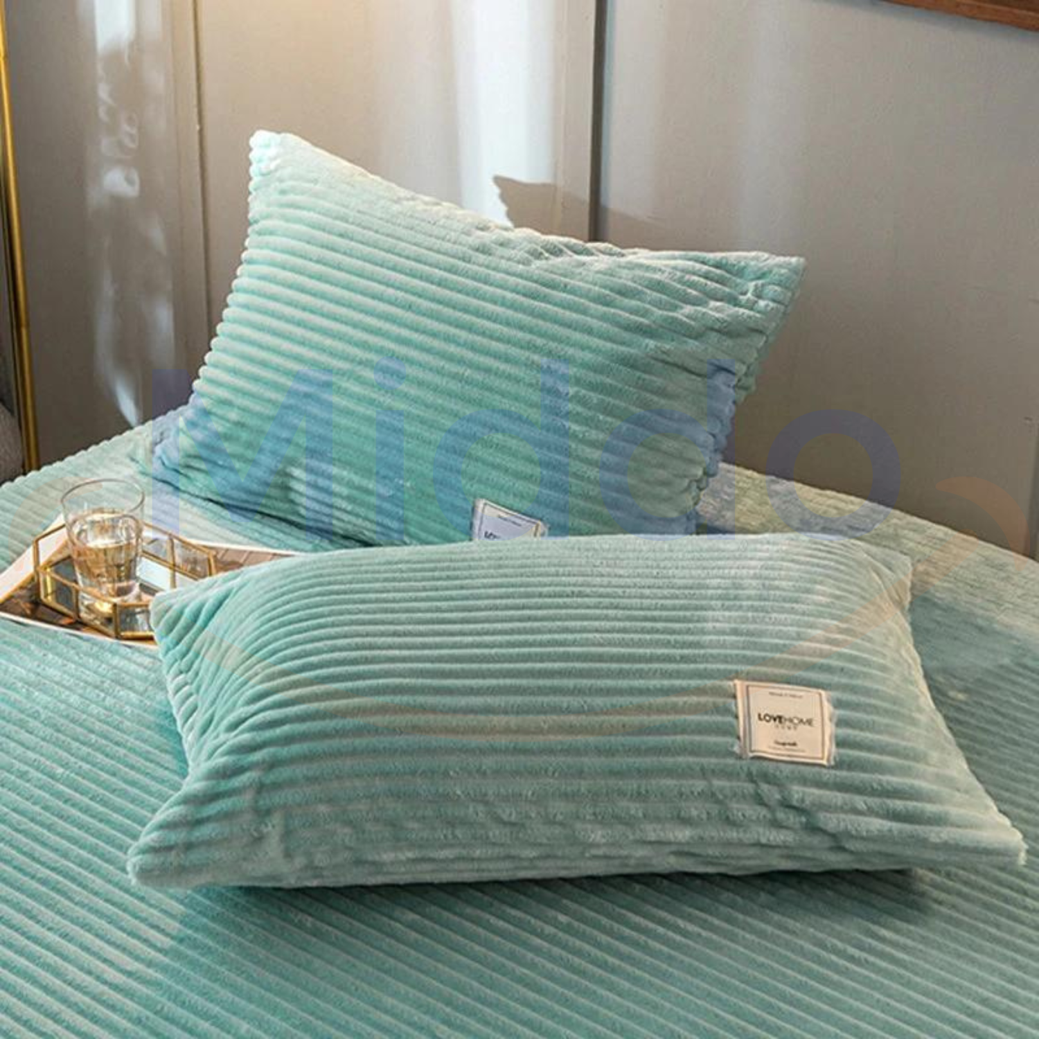 Jadegrüne, samtige Fleece-Kissen auf dem Bett mit Glasdekoration.