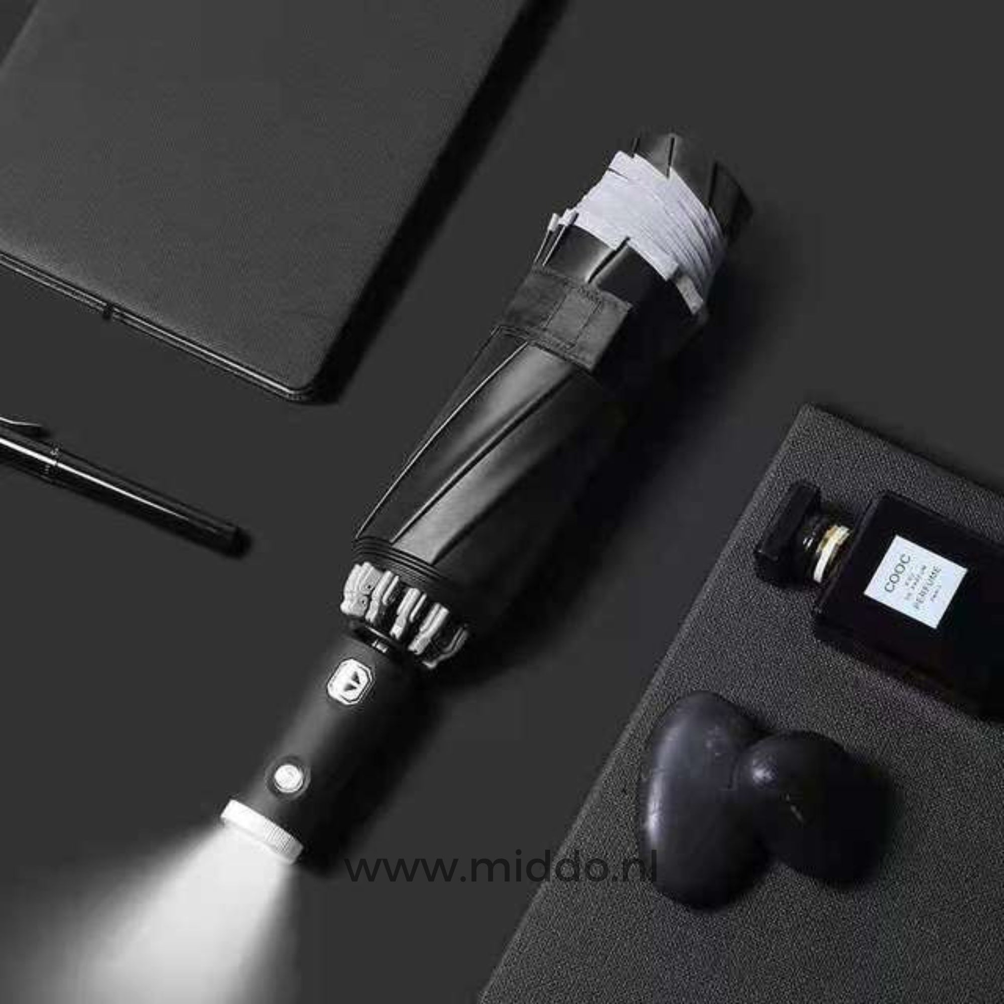 Schwarzer Regenschirm mit eingebauter Taschenlampe, umgeben von Alltagsgegenständen