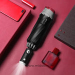 Schwarzer Regenschirm mit reflektierendem Rand auf rotem Hintergrund.