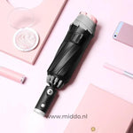 Schwarzer Regenschirm mit reflektierendem Rand, Handy und Stift auf rosa Hintergrund.