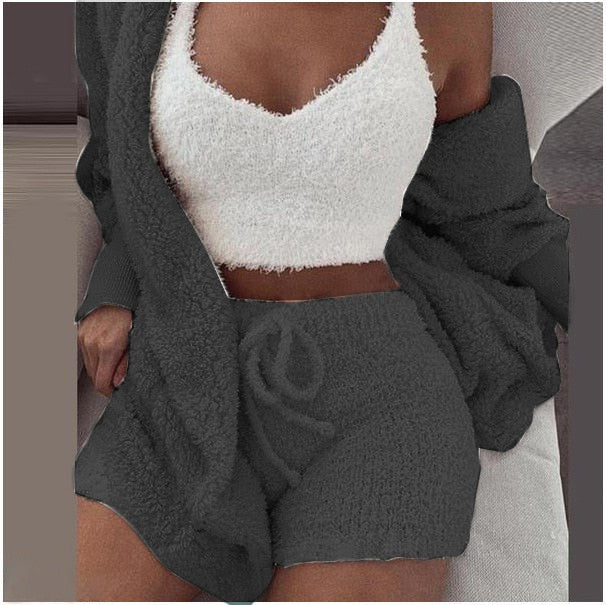 Frau in grauem SheCutie Bequem-Set mit Shorts, Top und Jacke sitzt auf der Couch.