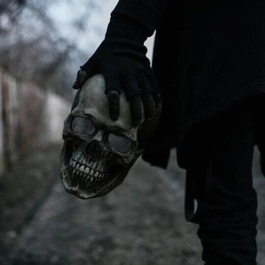 Hand hält ein Schädelmaske in dunkler Umgebung