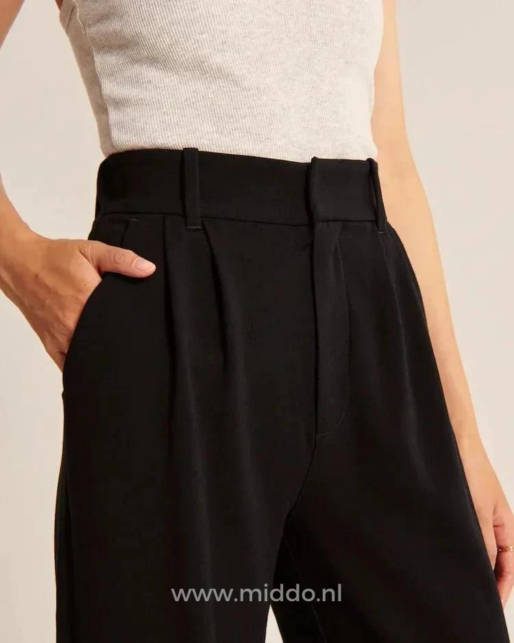 Foto einer Frau in einer schwarzen, weiten Hose, die von der Taille aus gesehen wird und ihre Hand in der Seitentasche hat.