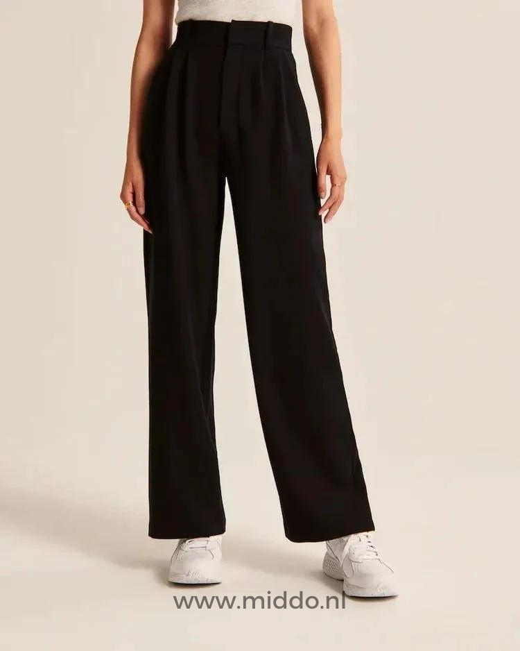 Eine Frau in weißen Sportschuhen zeigt die schwarze weite Hose.