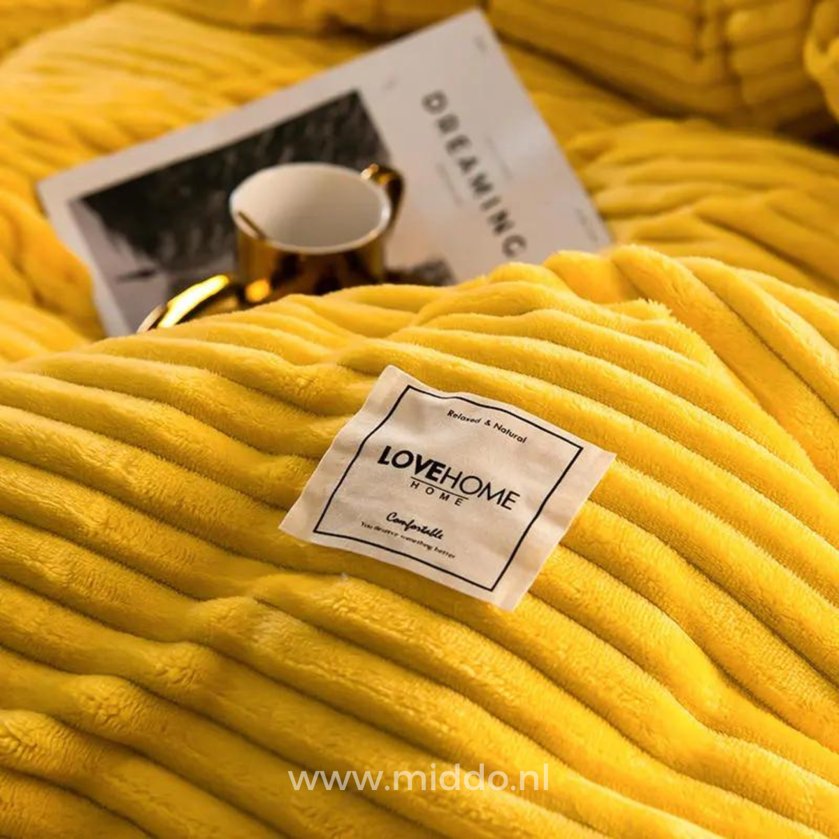 Gelbes Fleece-Bettüberwurf mit LOVEHOME-Label und Tasse.