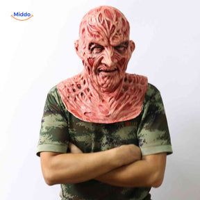 Zombiora Maske – Person mit verbranntem Gesicht, camo Shirt und verschränkten Armen, seitlich aufgenommen. Besuchen Sie uns auf www.middo.de