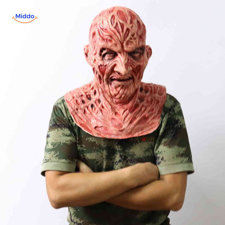 Zombiora Maske – Person mit verbranntem Gesicht, camo Shirt und verschränkten Armen, seitlich aufgenommen. Besuchen Sie uns auf www.middo.de