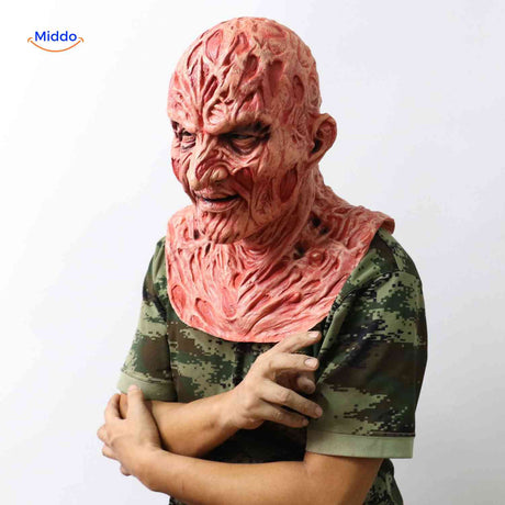 Die Zombiora-Maske - eine Person trägt eine verkohlte Gesichtsmaske, dazu ein Camouflage-Shirt und hat die Hand auf der Maske. Entdecken Sie mehr auf www.middo.de