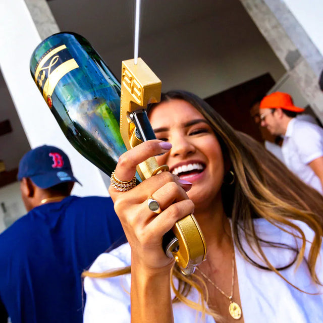 Lächelnde Frau auf einer Party mit goldfarbener Trinkpistole und Champagnerflasche