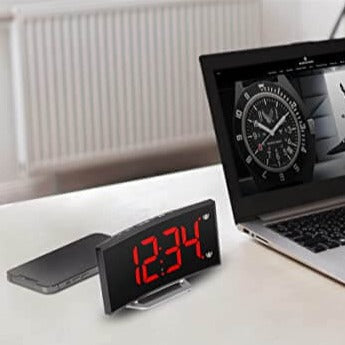 Digitale Wecker mit roter LED-Zeit neben einem Laptop.