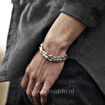 Man trägt ein silbernes Drachenarmband, die Hände in den Taschen einer dunklen Hose.