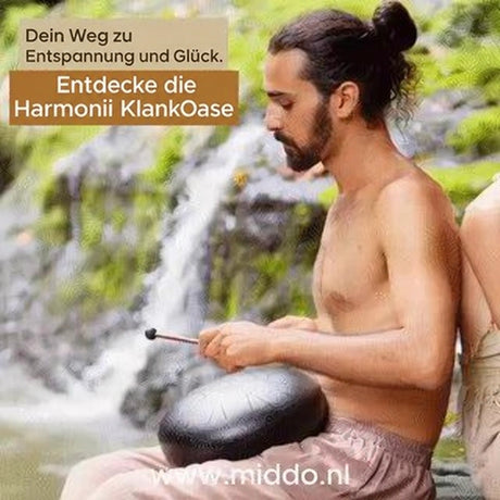 Mann spielt eine Harmonii Stahlzungentrommel vor einem Wasserfall.