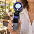 Palmora faltbarer Handventilator: graues Modell mit violettem Ring in einer Hand.
