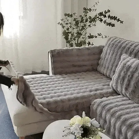 Frau legt einen grauen, plüschigen Sofaschoner auf ein Sofa