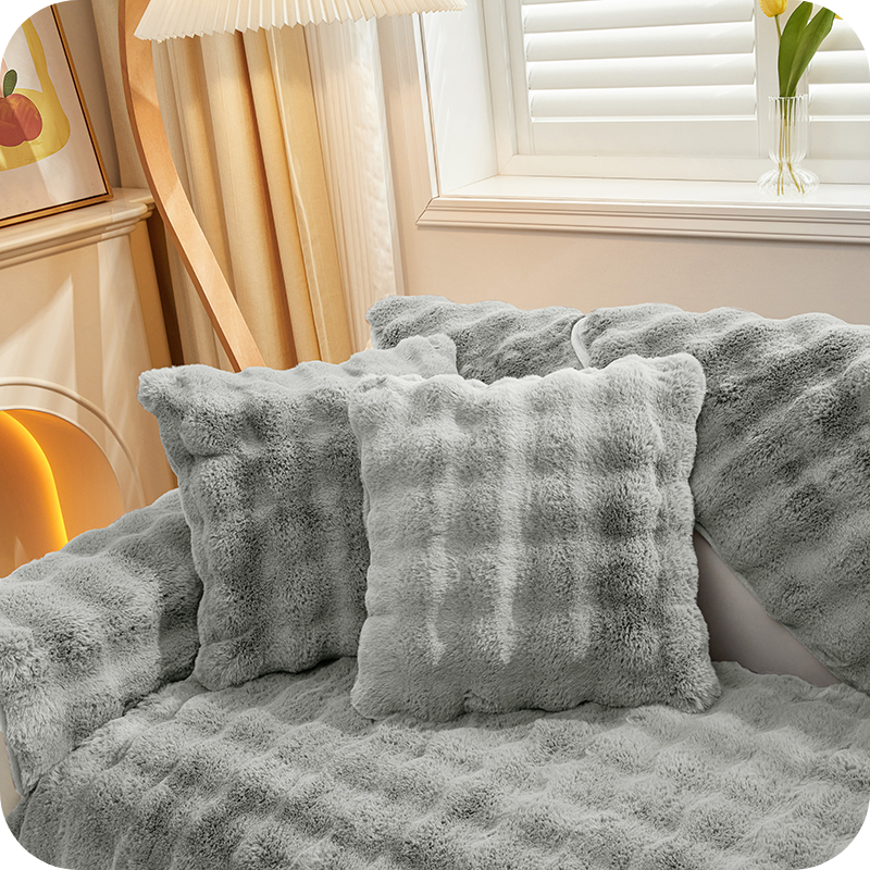 Grau Plüschkissen und Decken auf einer Couch bei einem Fenster