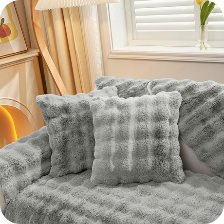 Grau Plüschkissen und Decken auf einer Couch bei einem Fenster