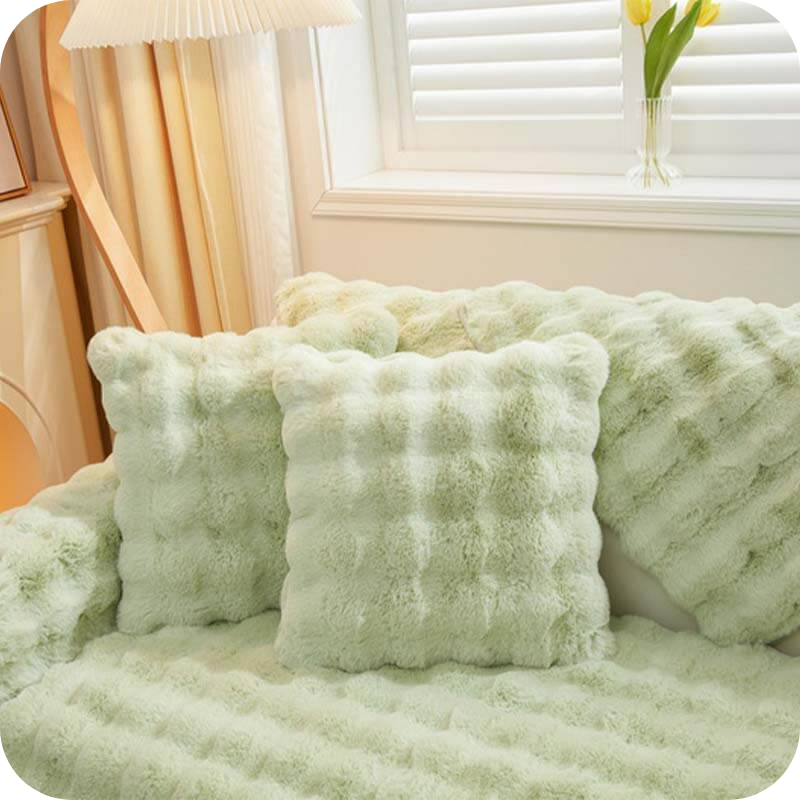 Grüne Plüschkissen und Decke auf einer Couch bei einem Fenster