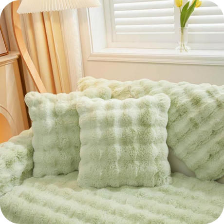 Grüne Plüschkissen und Decke auf einer Couch bei einem Fenster