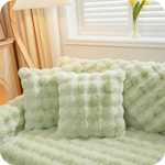 Grüne Plüschkissen und Decke auf einer Couch bei einem Fenster