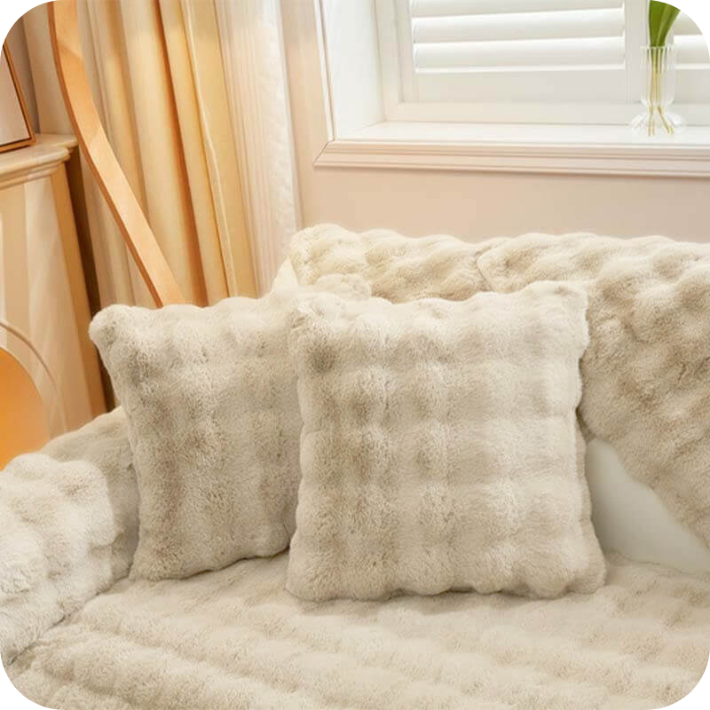 Weiße Plüschkissen und eine Decke auf einem hellen Sofa