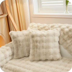 Weiße Plüschkissen und eine Decke auf einem hellen Sofa