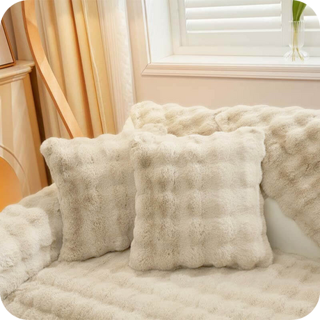 Weiße Plüschkissen und eine Decke auf einem hellen Sofa