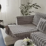 Frau legt einen grauen, plüschigen Sofaschoner auf ein Sofa